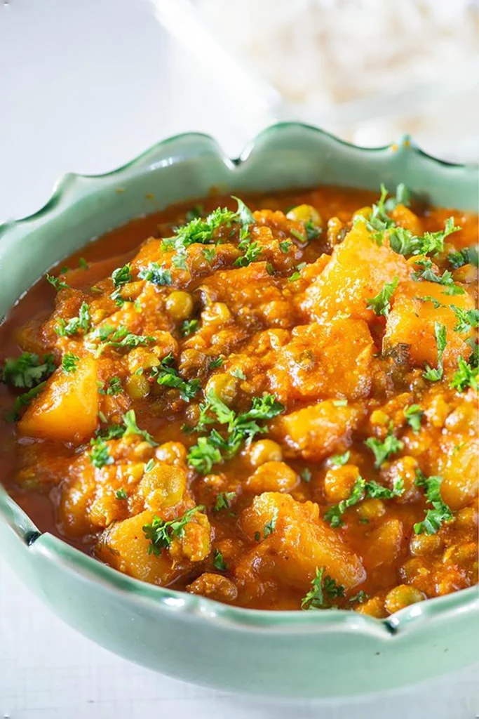 Bowl of aloo matar potato and peas curry garnished with cilantro.